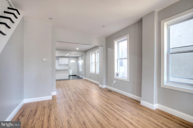 unfurnished living room with light wood-type flooring, baseboards, and stairs