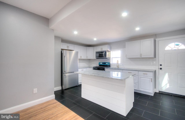 kitchen featuring light stone counters, appliances with stainless steel finishes, a kitchen island, and white cabinetry