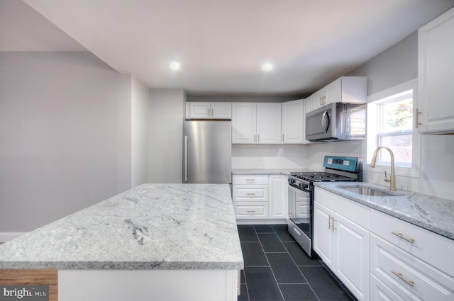 kitchen with a kitchen island, light stone countertops, stainless steel appliances, white cabinetry, and a sink