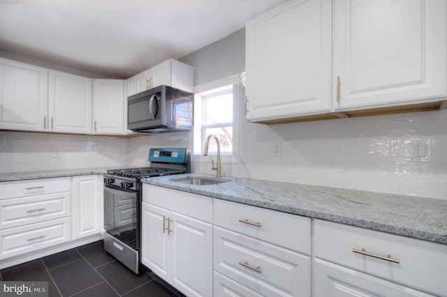 kitchen with light stone counters, white cabinets, stainless steel range with gas stovetop, a sink, and dark tile patterned floors