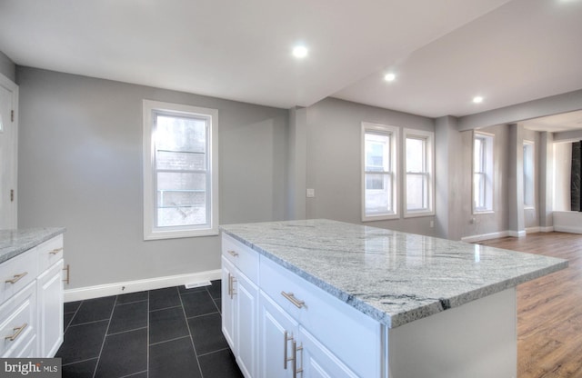 kitchen with light stone counters, recessed lighting, a kitchen island, baseboards, and white cabinets