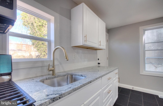 kitchen featuring light stone countertops, decorative backsplash, white cabinets, and a sink