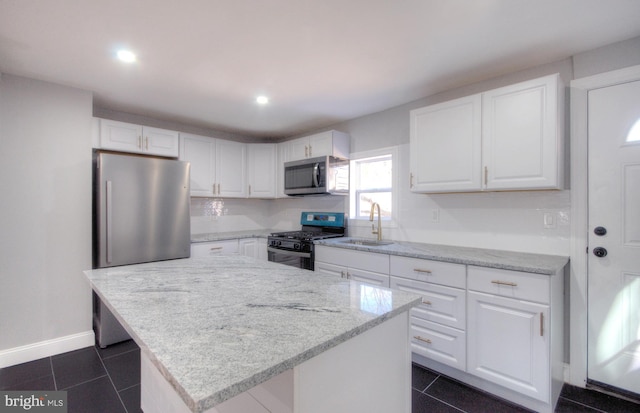 kitchen featuring stainless steel appliances, dark tile patterned floors, a sink, white cabinets, and a center island