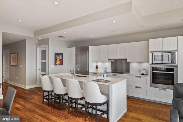 kitchen featuring stainless steel appliances, white cabinetry, a center island with sink, and a kitchen bar