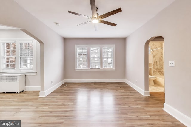 empty room with arched walkways, light wood-type flooring, and baseboards