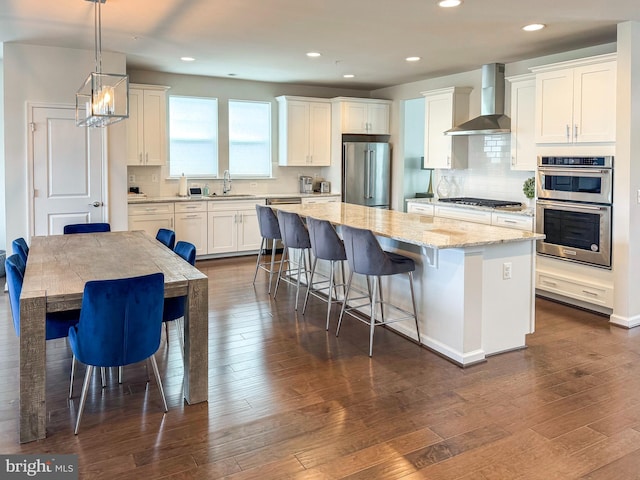 kitchen with stainless steel appliances, a kitchen island, a sink, wall chimney range hood, and dark wood-style floors