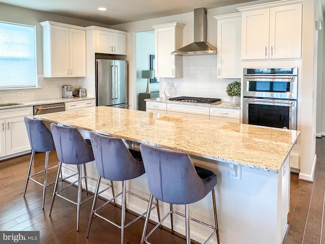 kitchen with dark wood-style flooring, appliances with stainless steel finishes, white cabinets, a kitchen island, and wall chimney range hood