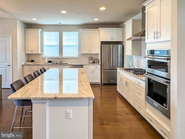 kitchen featuring a breakfast bar, backsplash, appliances with stainless steel finishes, a sink, and wall chimney exhaust hood