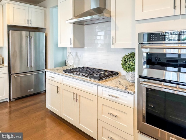 kitchen featuring tasteful backsplash, wall chimney exhaust hood, wood finished floors, stainless steel appliances, and white cabinetry