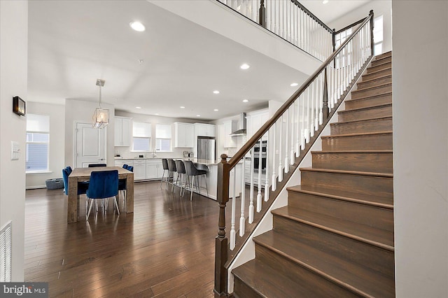 staircase featuring a towering ceiling, visible vents, hardwood / wood-style floors, and recessed lighting