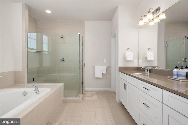 full bath with a stall shower, vanity, baseboards, and a bath