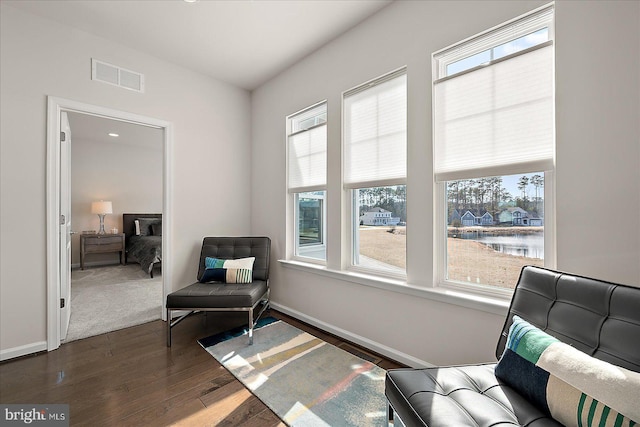 sitting room featuring a water view, baseboards, visible vents, and dark wood-style flooring