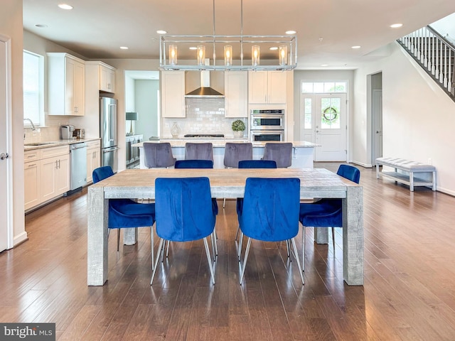 kitchen with a sink, a kitchen island, appliances with stainless steel finishes, wall chimney range hood, and dark wood-style floors