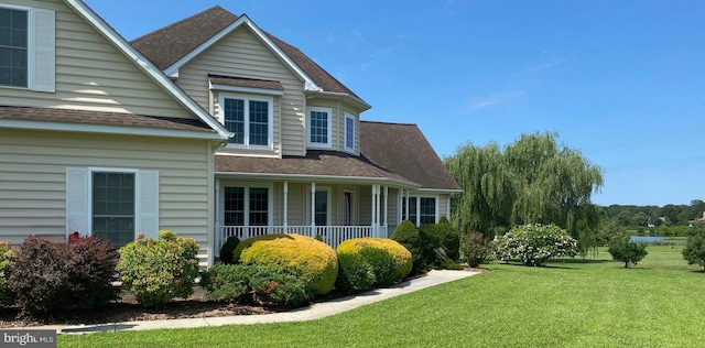 view of side of home featuring roof with shingles, a porch, and a yard