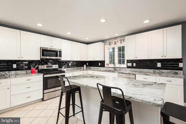 kitchen with a breakfast bar area, stainless steel appliances, light tile patterned flooring, a sink, and white cabinetry