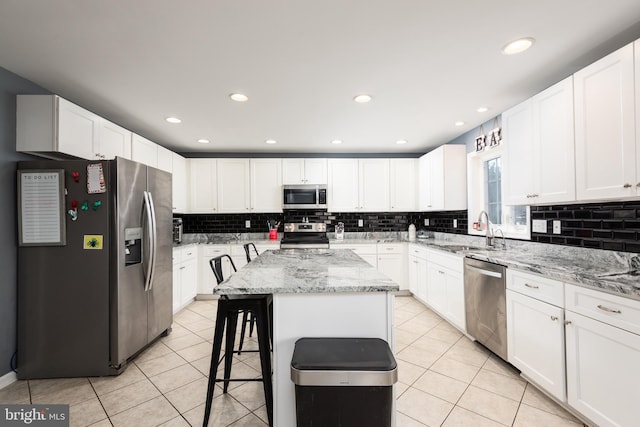 kitchen with light tile patterned floors, a sink, appliances with stainless steel finishes, a center island, and tasteful backsplash