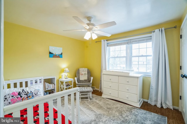 bedroom featuring ceiling fan, a nursery area, wood finished floors, and baseboards