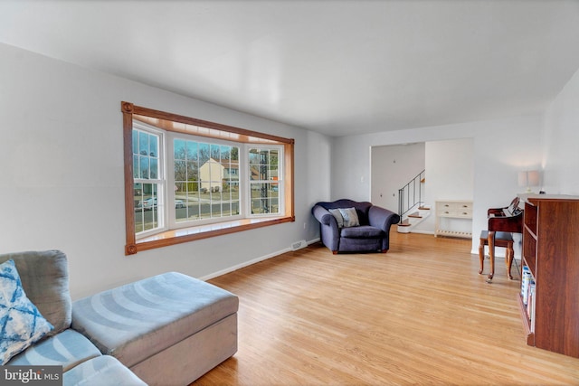 living area featuring light wood finished floors, stairway, and baseboards