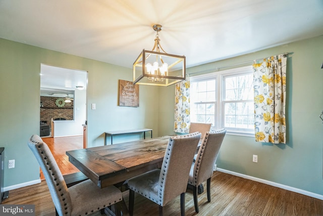 dining room featuring a notable chandelier, a fireplace, wood finished floors, and baseboards