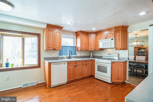 kitchen featuring light wood finished floors, light countertops, visible vents, a sink, and white appliances