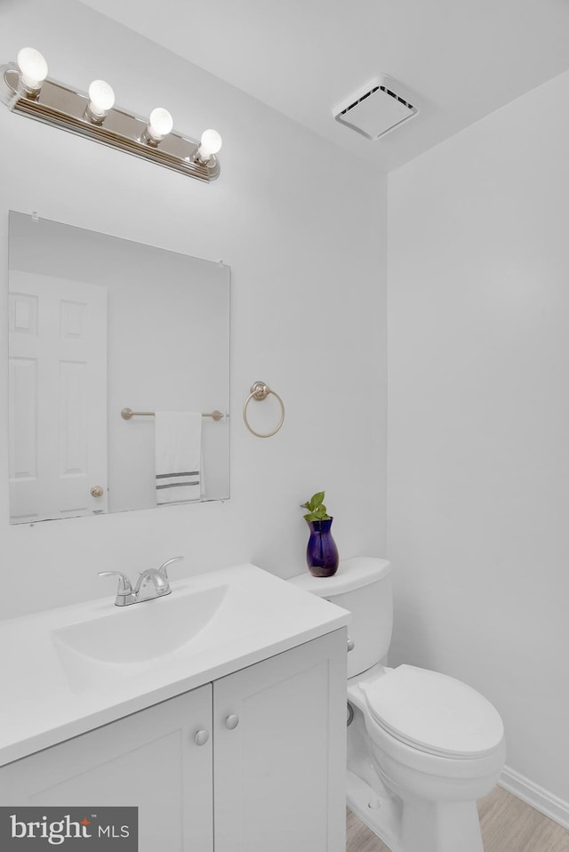 half bathroom with toilet, visible vents, wood finished floors, and vanity