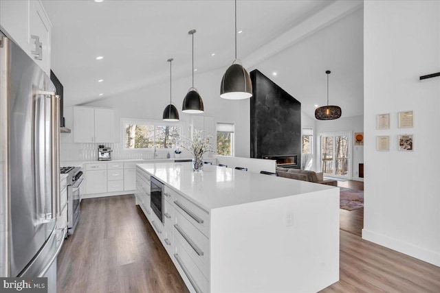 kitchen featuring premium appliances, a kitchen island, light countertops, white cabinetry, and pendant lighting