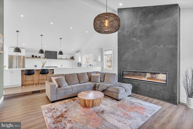 living area with a large fireplace, high vaulted ceiling, recessed lighting, and light wood-style floors