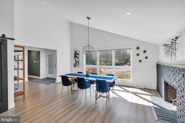 dining space with light wood finished floors, a barn door, a brick fireplace, high vaulted ceiling, and baseboards