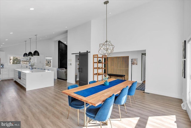 dining area with light wood finished floors, high vaulted ceiling, a barn door, and baseboards