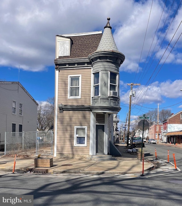 view of front of home featuring mansard roof, a shingled roof, and fence