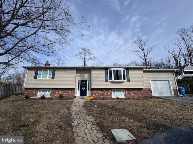 bi-level home with brick siding, fence, a chimney, and an attached garage