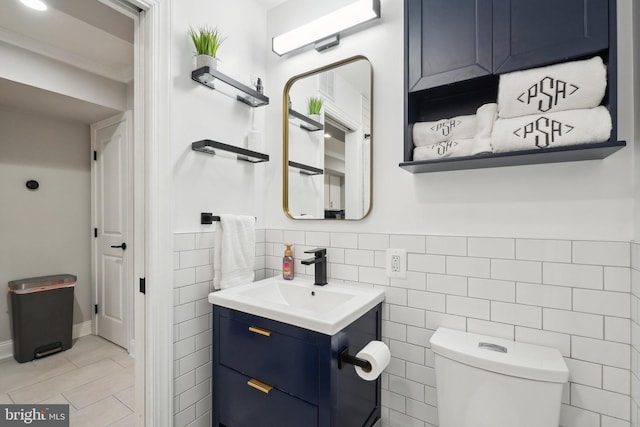 bathroom with wainscoting, toilet, ornamental molding, vanity, and tile walls