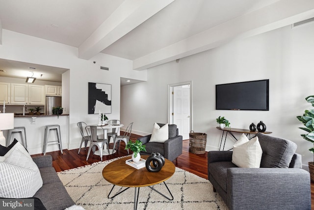 living area with beam ceiling, visible vents, baseboards, and wood finished floors