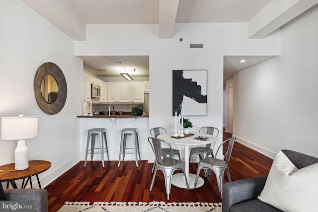 dining area featuring visible vents, baseboards, beamed ceiling, and wood finished floors