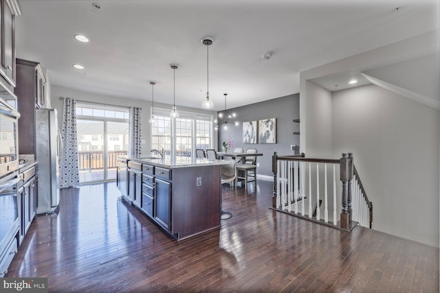 kitchen with dark wood-style flooring, hanging light fixtures, freestanding refrigerator, a kitchen island with sink, and a kitchen breakfast bar