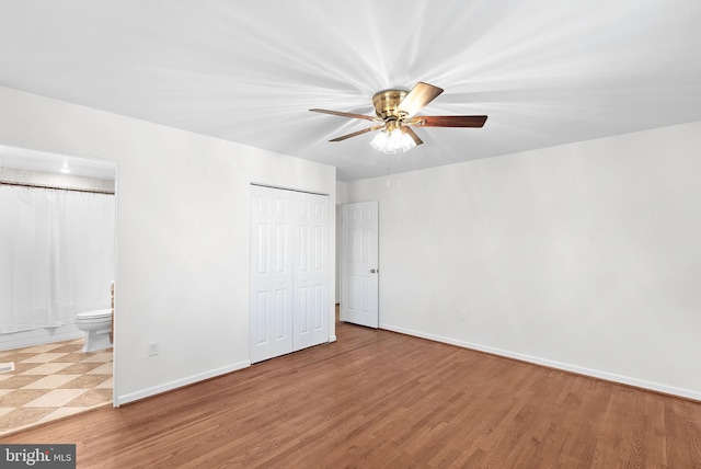 unfurnished bedroom featuring a closet, connected bathroom, baseboards, and wood finished floors