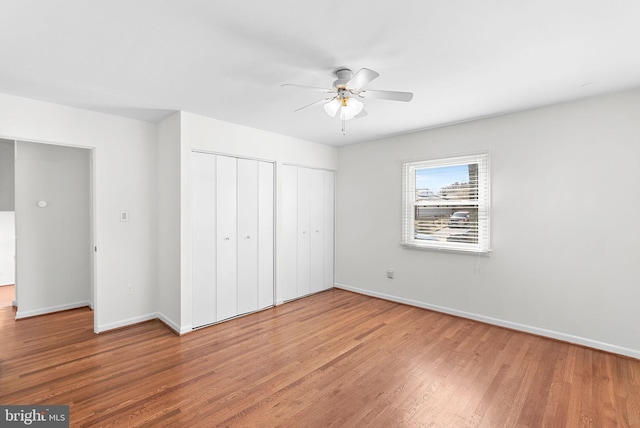 unfurnished bedroom with baseboards, ceiling fan, wood finished floors, and multiple closets