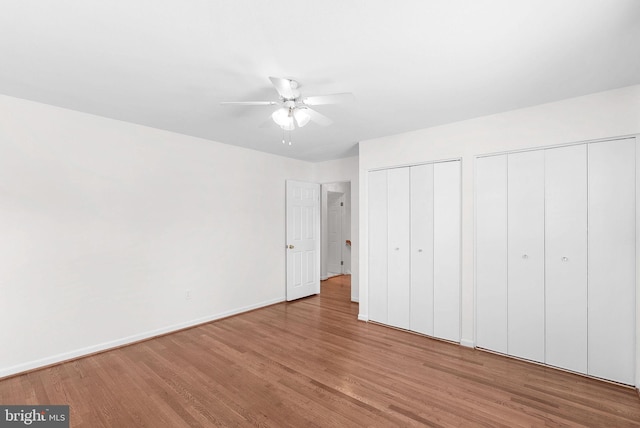 unfurnished bedroom with ceiling fan, wood finished floors, two closets, and baseboards