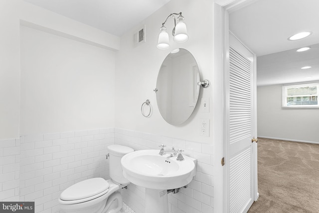 half bathroom featuring tile walls, recessed lighting, visible vents, toilet, and wainscoting