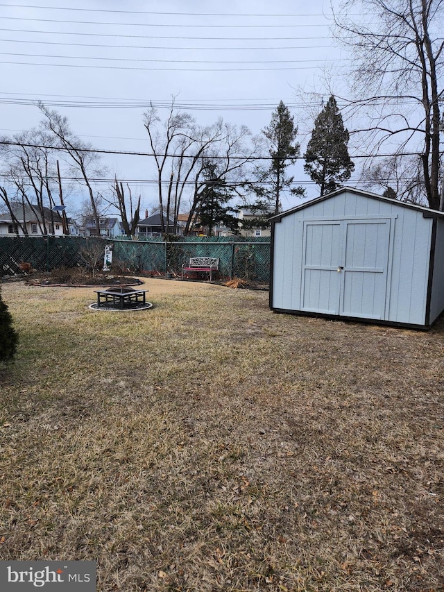 view of yard with a storage shed, a fenced backyard, a fire pit, and an outbuilding