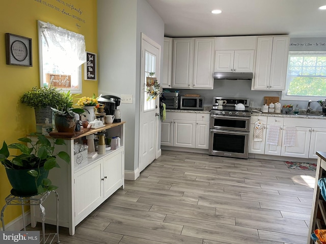 kitchen featuring under cabinet range hood, stainless steel appliances, wood finish floors, a sink, and white cabinets