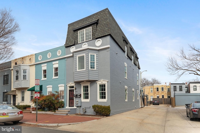 view of front of house with brick siding, roof with shingles, and mansard roof