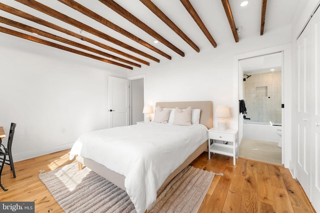 bedroom featuring light wood-type flooring, baseboards, connected bathroom, and beamed ceiling