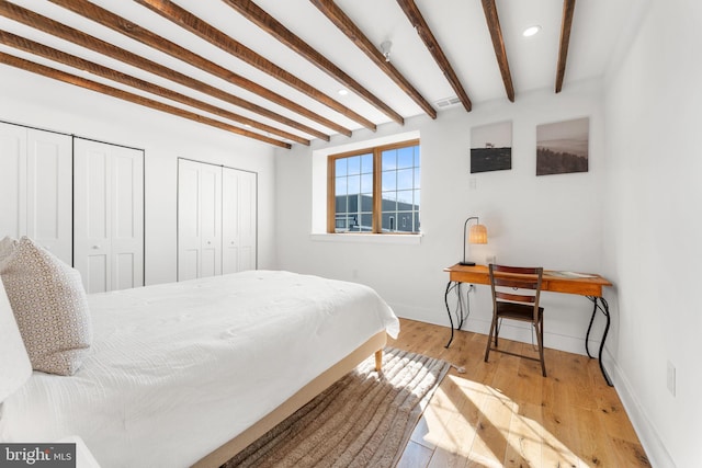 bedroom featuring wood-type flooring, baseboards, beam ceiling, and two closets