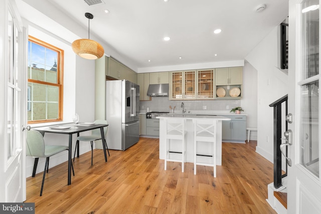 kitchen with under cabinet range hood, a kitchen island, light countertops, appliances with stainless steel finishes, and backsplash