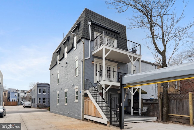 view of front of property featuring mansard roof, a balcony, brick siding, fence, and stairway