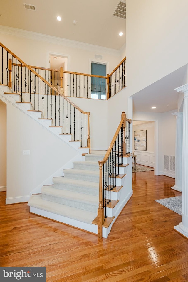 stairway with visible vents, crown molding, a high ceiling, and wood finished floors