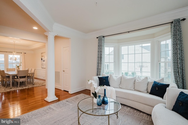 living area featuring a tray ceiling, crown molding, decorative columns, visible vents, and wood finished floors