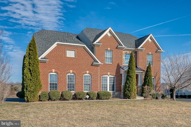 view of front of property featuring a front yard, brick siding, and roof with shingles