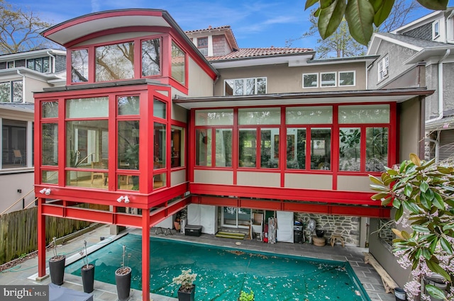 rear view of property featuring a tiled roof, stucco siding, a sunroom, and a fenced in pool